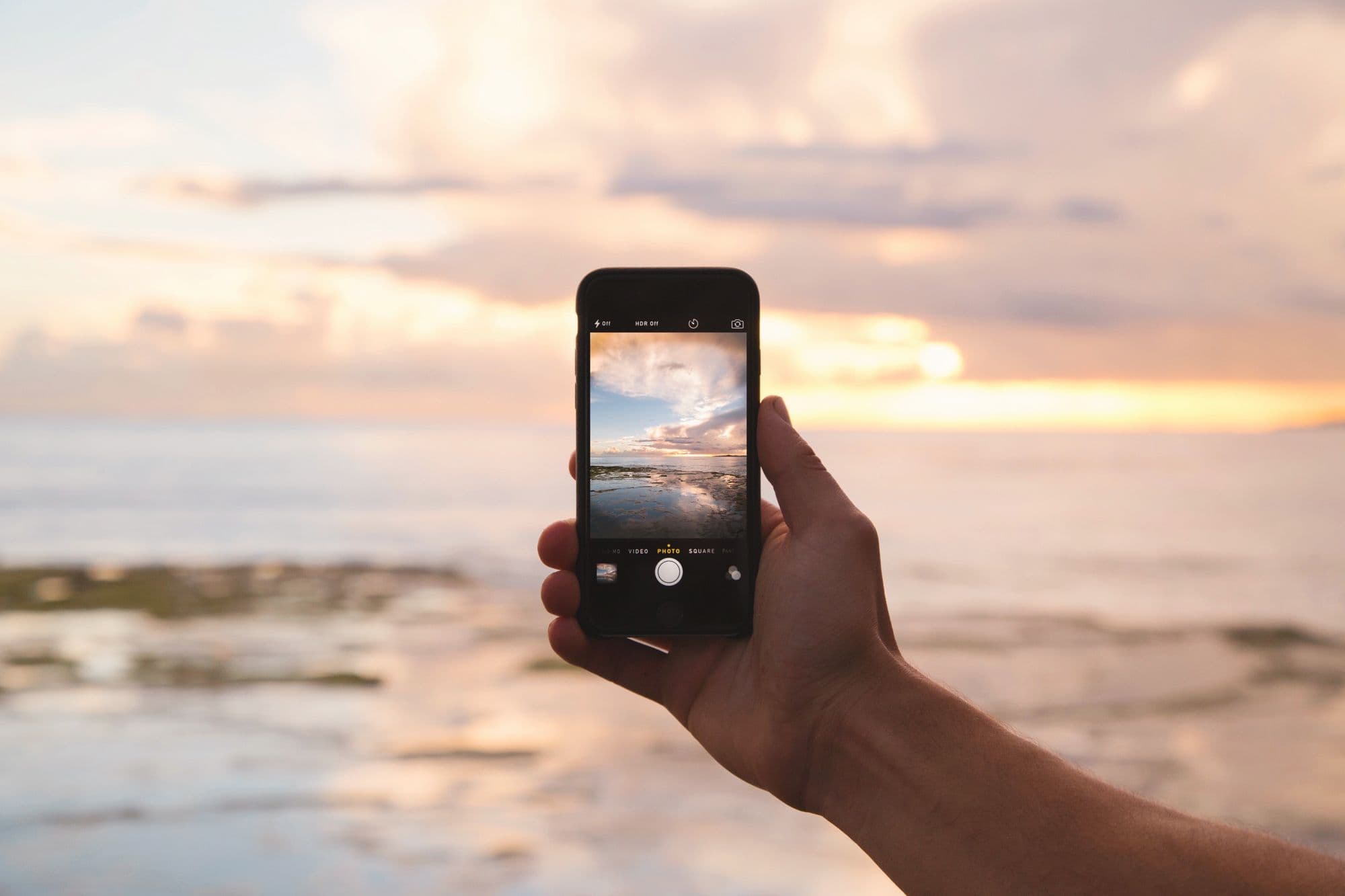 Mano sosteniendo un teléfono frente al mar al atardecer